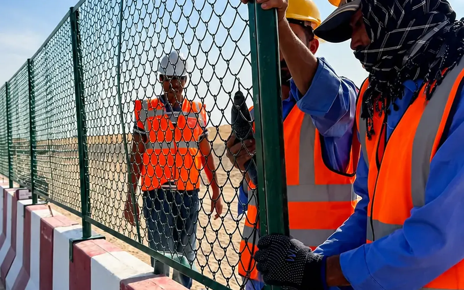 Chain-Link Safety Fence and Concrete Barrier Installation in the UAE Workers installing chain-link safety fencing on concrete barriers at a UAE project site