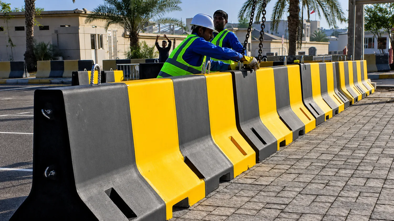 Workers positioning black and yellow concrete barriers during a UAE site installation
