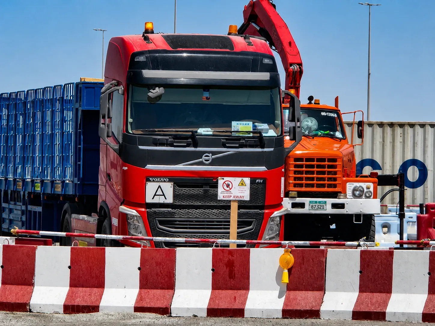 Heavy transport fleet and crane trucks coordinated behind temporary road barriers in the UAE