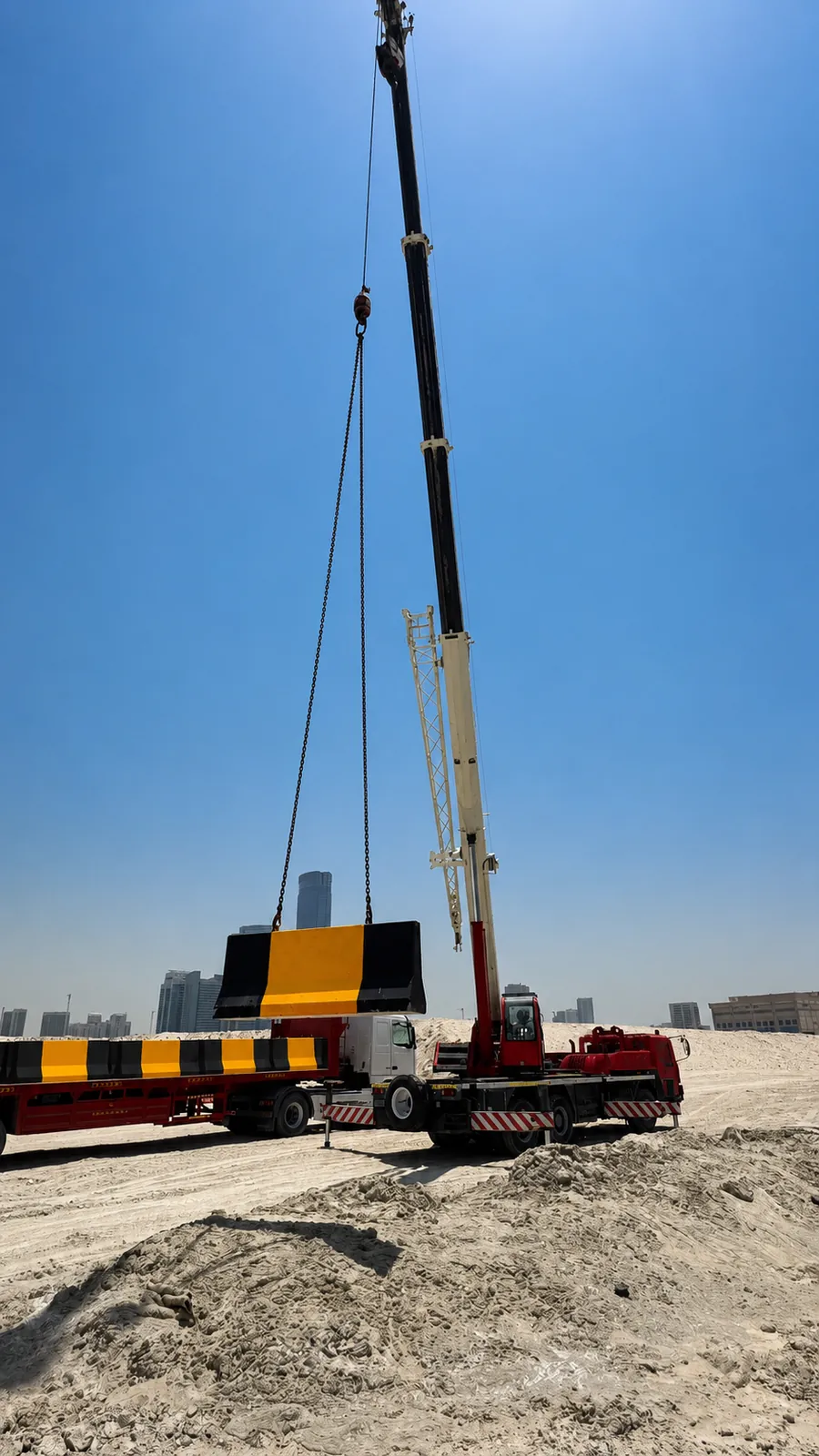 Mobile crane lifting a black and yellow concrete traffic barrier at a UAE construction site