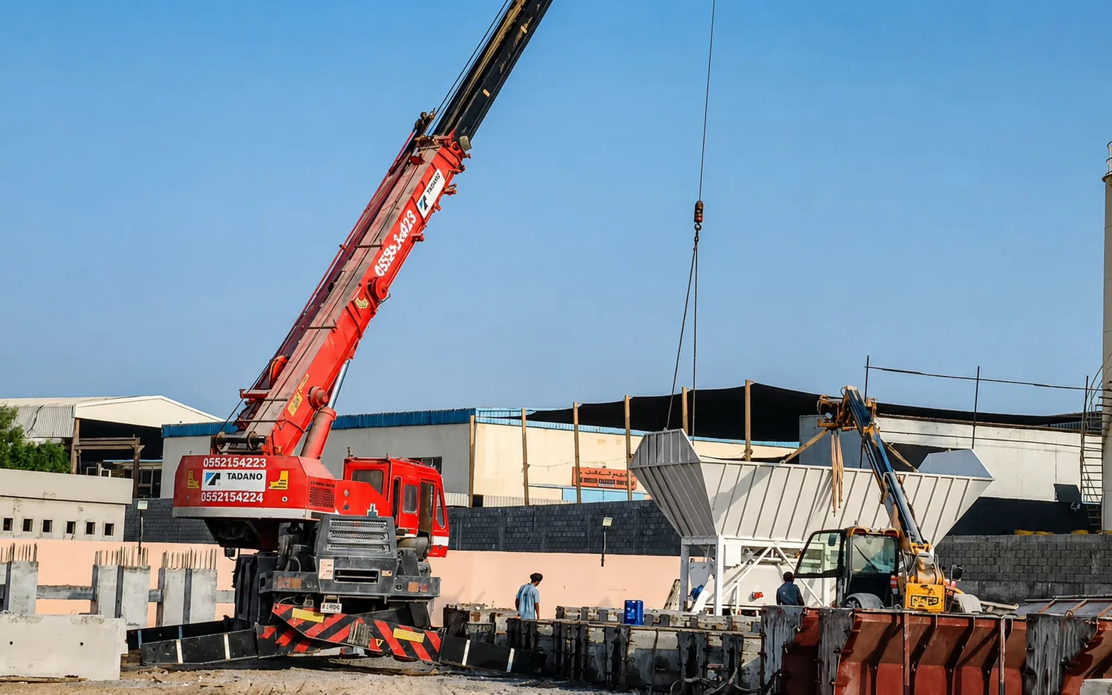 Red Tadano mobile crane performing a lifting operation in a precast concrete yard