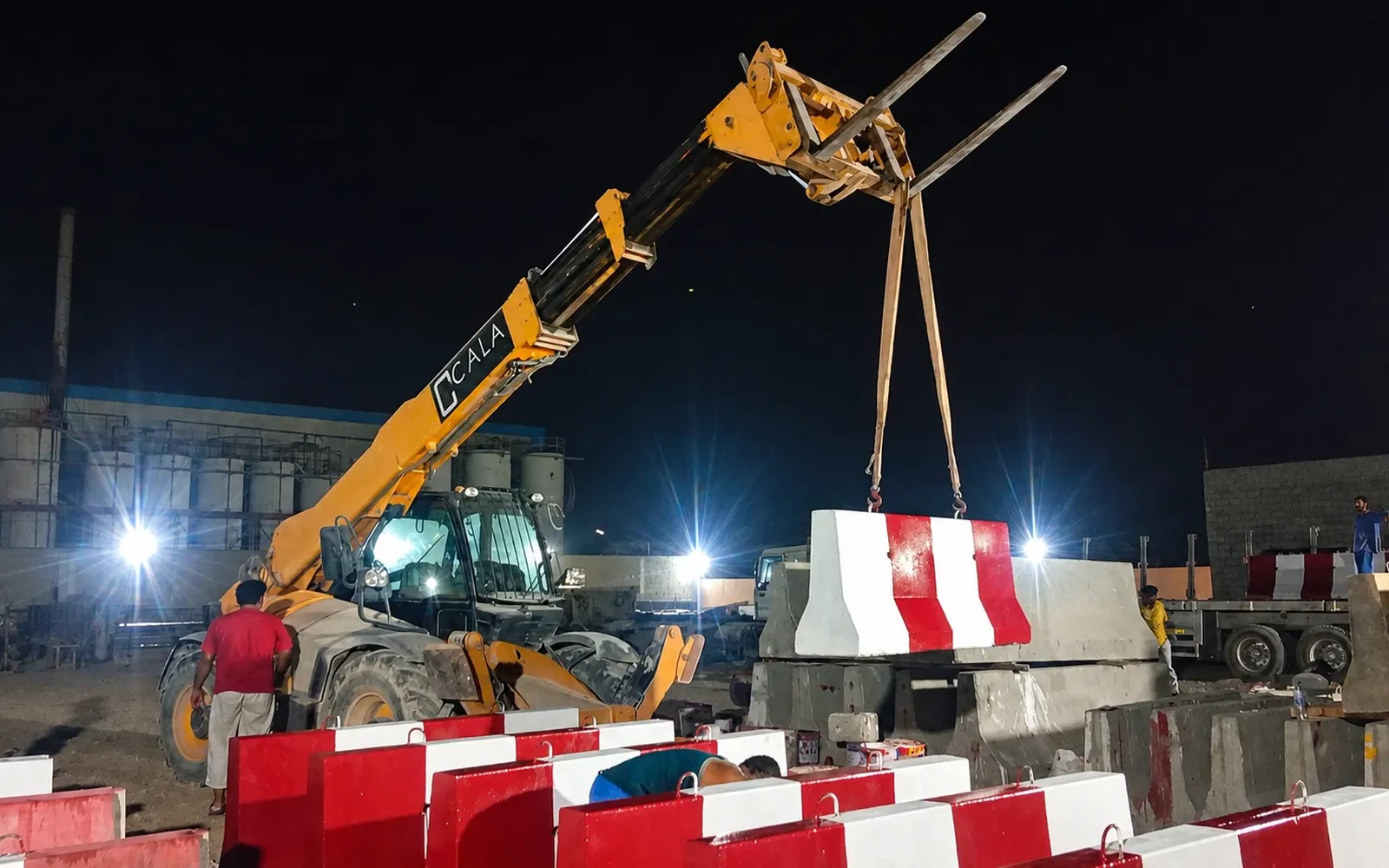 Night Concrete Barrier Installation with Telehandler in the UAE Telehandler lifting a red-and-white precast concrete road barrier during night installation in the UAE