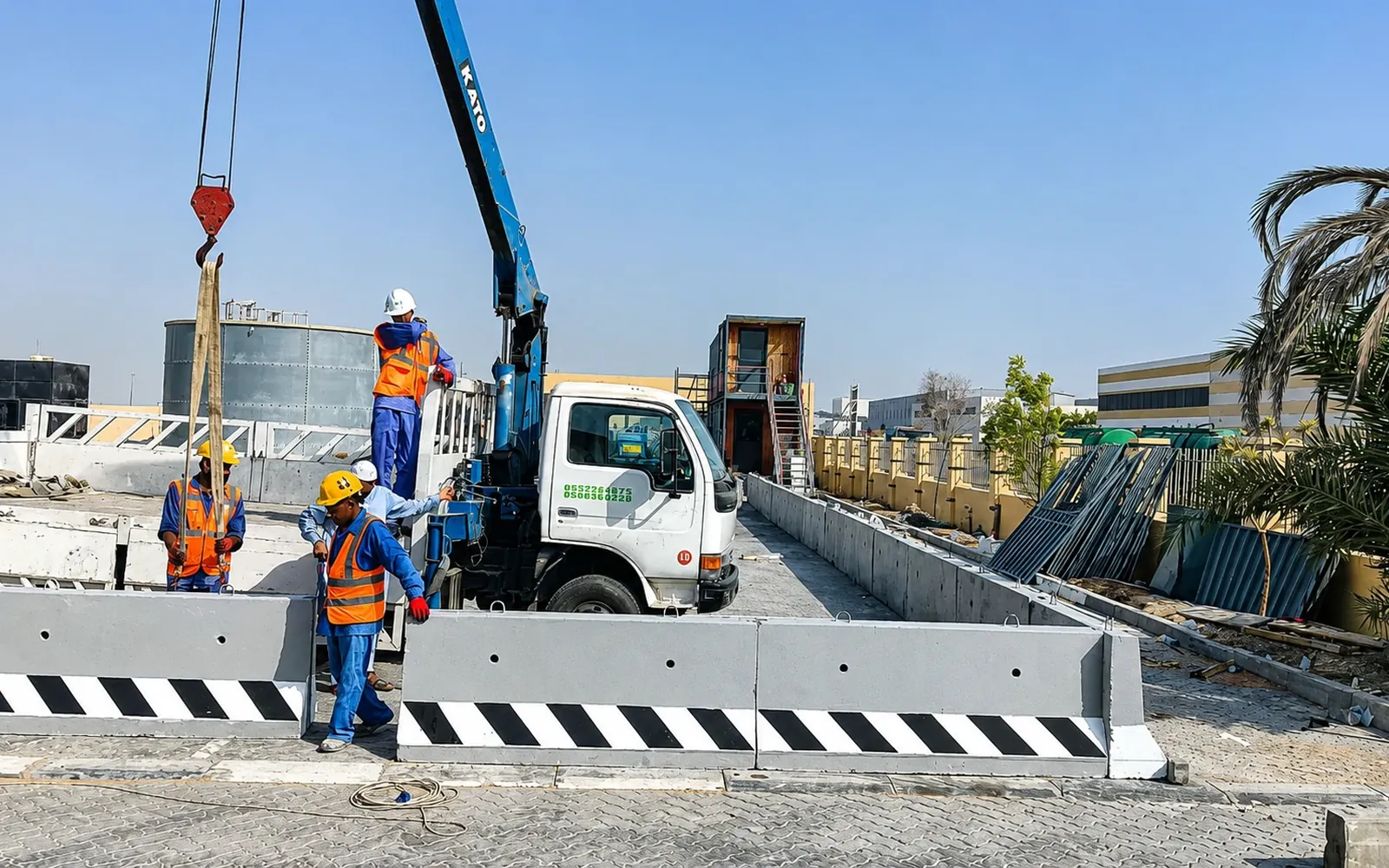 Truck-mounted crane positioning precast concrete barriers at a UAE project site